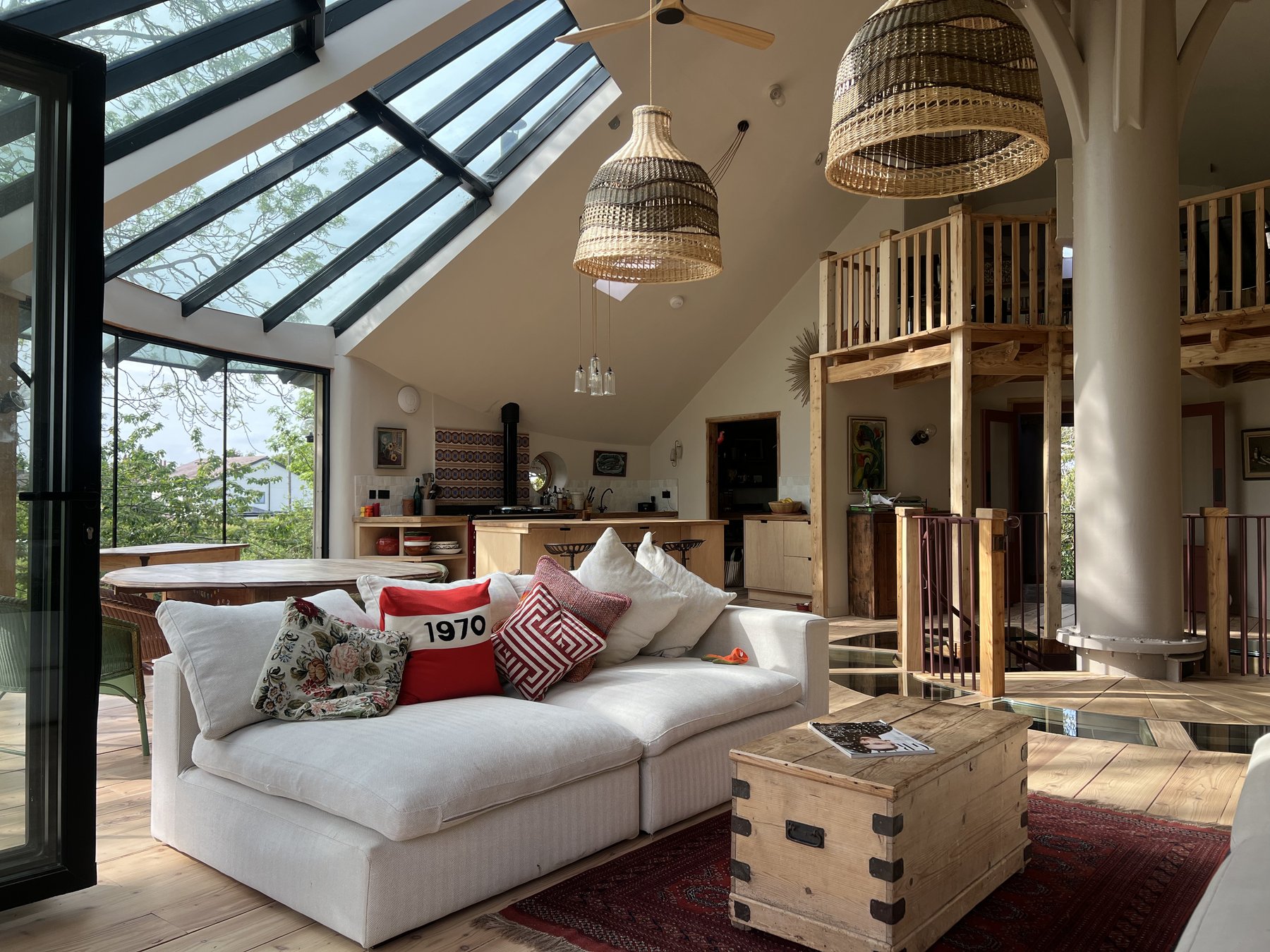 Open-plan living area with sectional sofa, vaulted ceiling, glazed walls, pendants and the mezzanine to the right