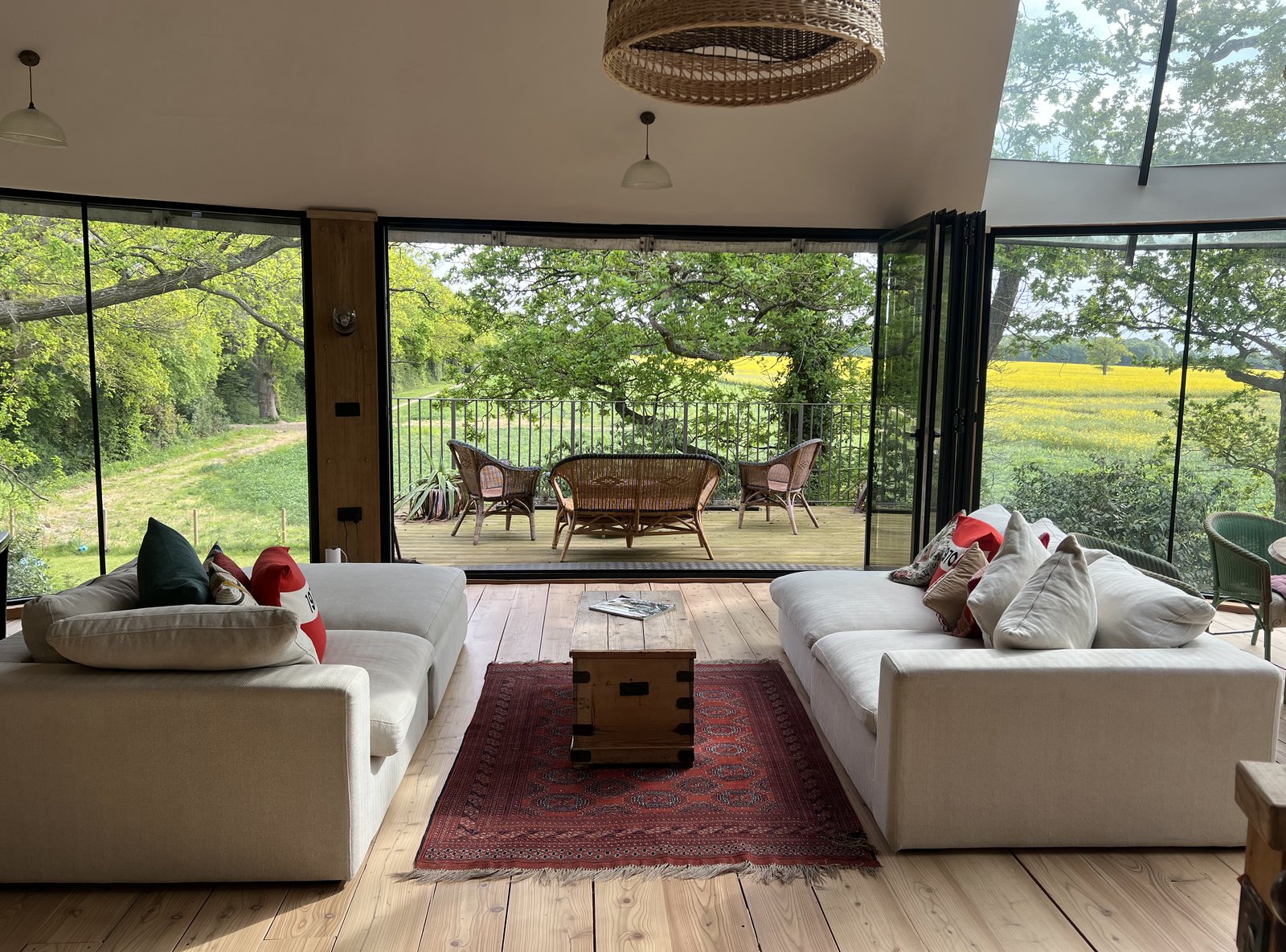 Living area with two cream sofas framing trifold doors that open onto a balcony overlooking wheat fields