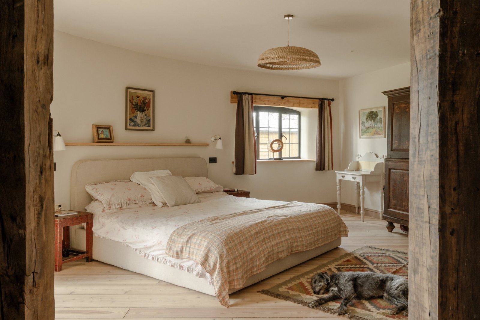 Principal bedroom with reclaimed timber beams, neutral palette, kilim rug and natural light from a leaded window