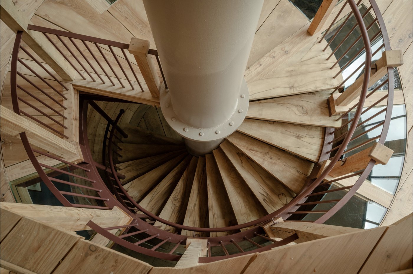 Spiral open-tread larch and ash staircase wrapping around the central reclaimed-steel column